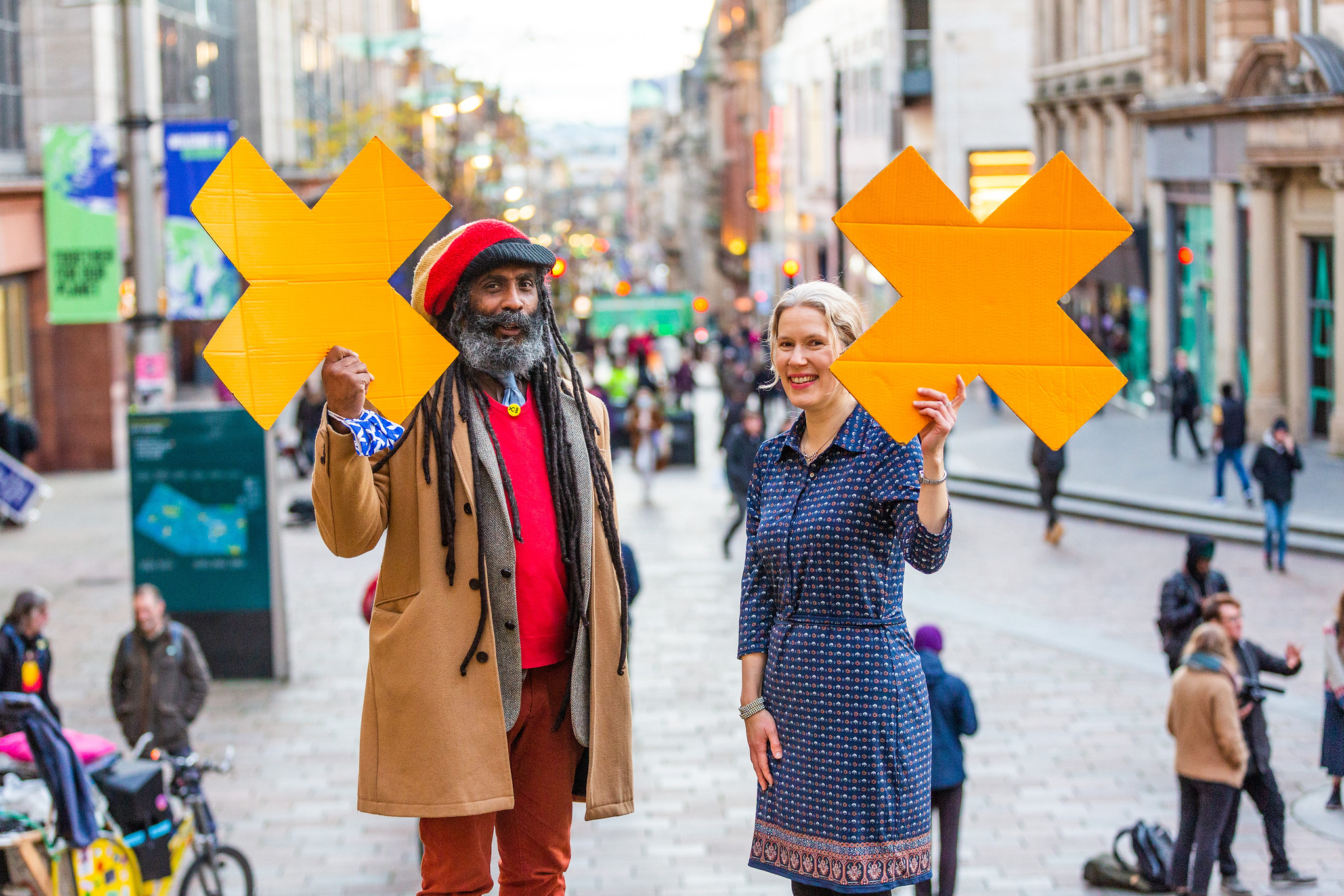 A Black man and a white woman hold bright orange X signs while smiling at the camera.